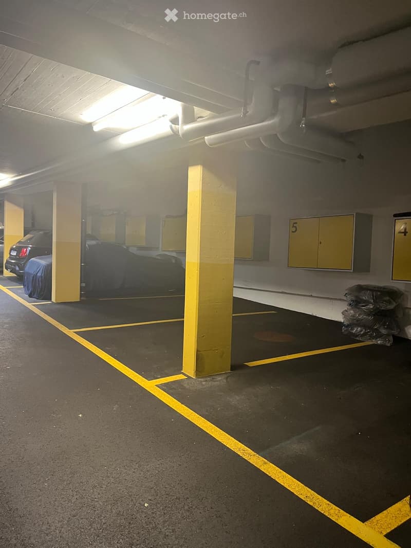 Underground parking area with marked parking spaces, covered vehicles, and numbered storage units.