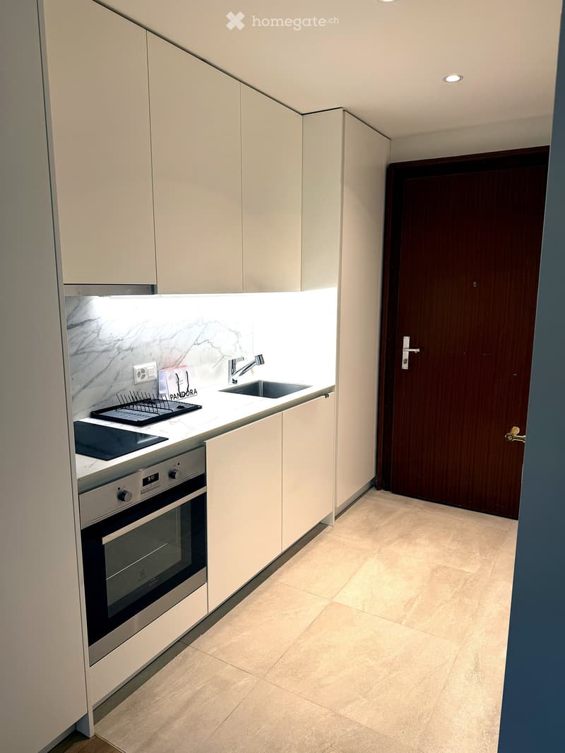 Modern kitchen with white cabinets, marble backsplash, stainless steel oven, sink, and faucet. Features a built-in lighting strip above the sink.