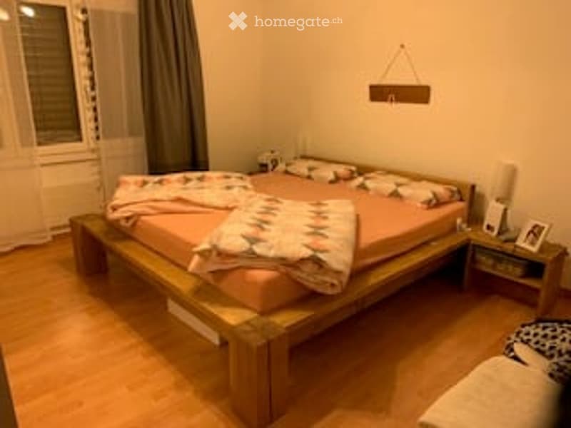 Cozy bedroom with wooden bed, pink bedding, nightstand with lamp, and a small picture frame on the nightstand.