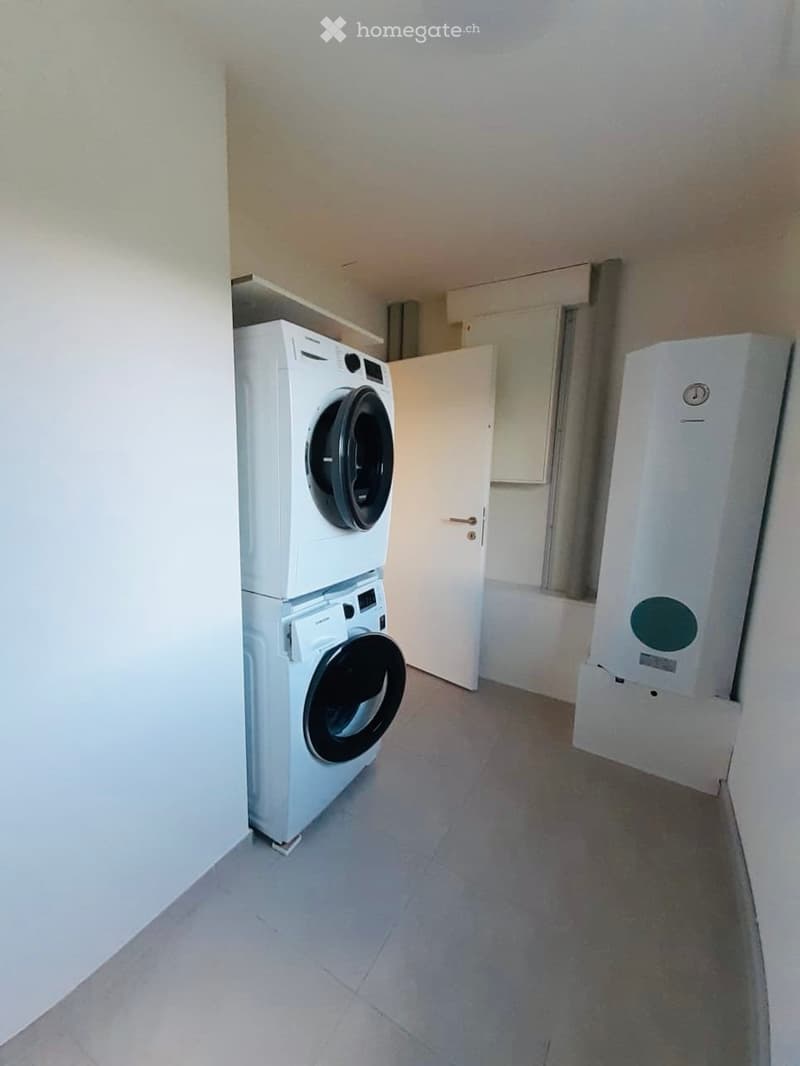 A small, clean utility room with a stacked washing machine and dryer, a water heater, and a door leading to another area.