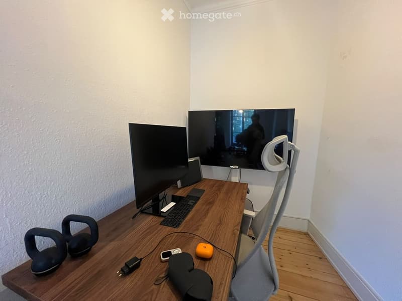 A modern workspace with a wooden desk, ergonomic chair, dual screens, keyboard, mouse, and various tech accessories including headphones and a laptop.