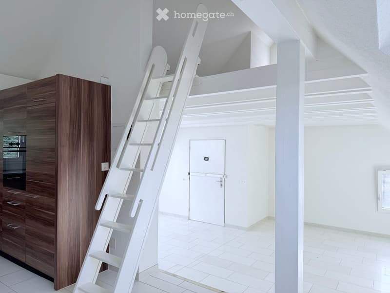 Bright, empty room with white tiled flooring, white walls, and a white staircase leading upwards. A wooden cabinet is visible on the left side.