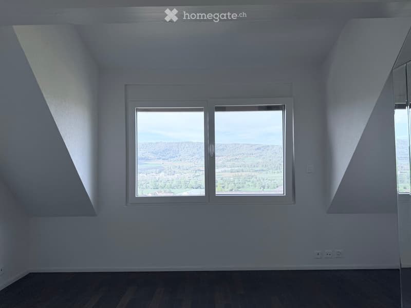 Empty room with wooden flooring, white walls, and large windows offering a scenic view of the landscape.