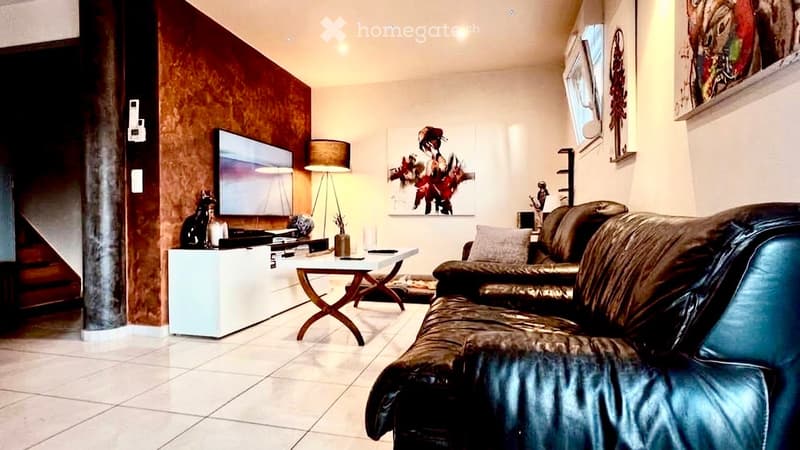 Modern living room with a dark leather sofa, a small wooden coffee table, a floor lamp, a TV on a white stand, and decorative art pieces on the walls.