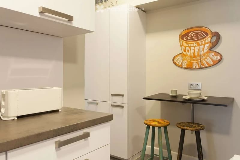 Modern kitchen with white cabinets, a countertop, a toaster, and a small dining area with two stools and a table.