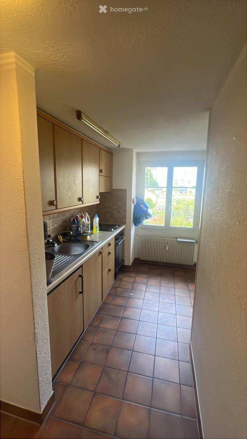 Kitchen with tiled floor, wooden cabinets, sink, oven, and radiator near window.