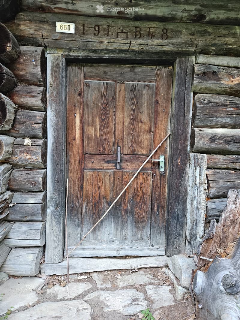 A rustic wooden door on a log cabin with weathered wood and stacked logs around it.