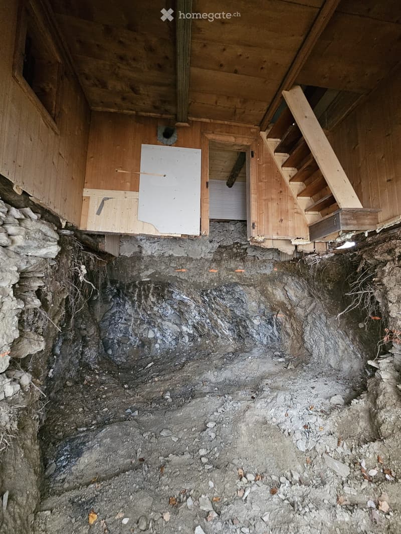 Raised wooden structure with visible staircase and foundation, surrounded by excavated soil and rocks.