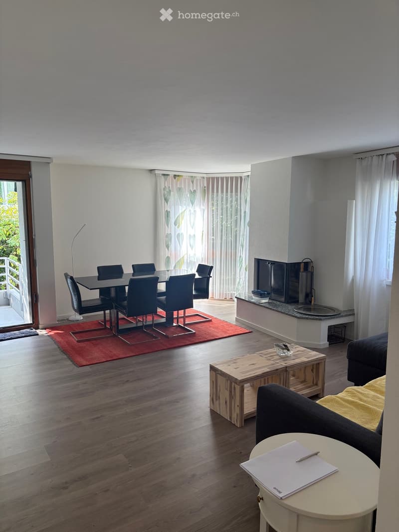 Modern living and dining area with wooden flooring, a sofa, coffee table, round table, dining table with chairs, and a screen. Features large windows with curtains and a balcony access.