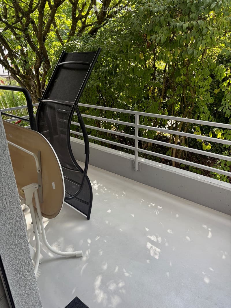 Balcony with white floor, metal railing, and outdoor furniture including a black mesh chair and a small table.
