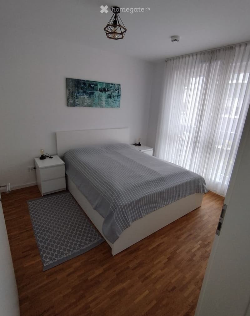Modern bedroom with a large bed, nightstands, a painting on the wall, and a patterned rug on the wooden floor.