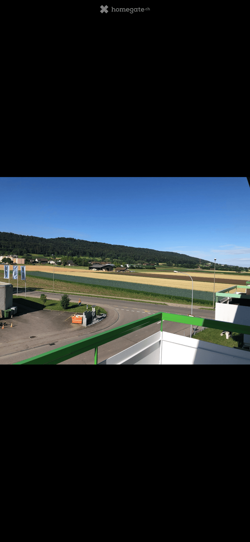 Balcony overlooking a parking lot, road, and rural landscape with fields and hills in the background.