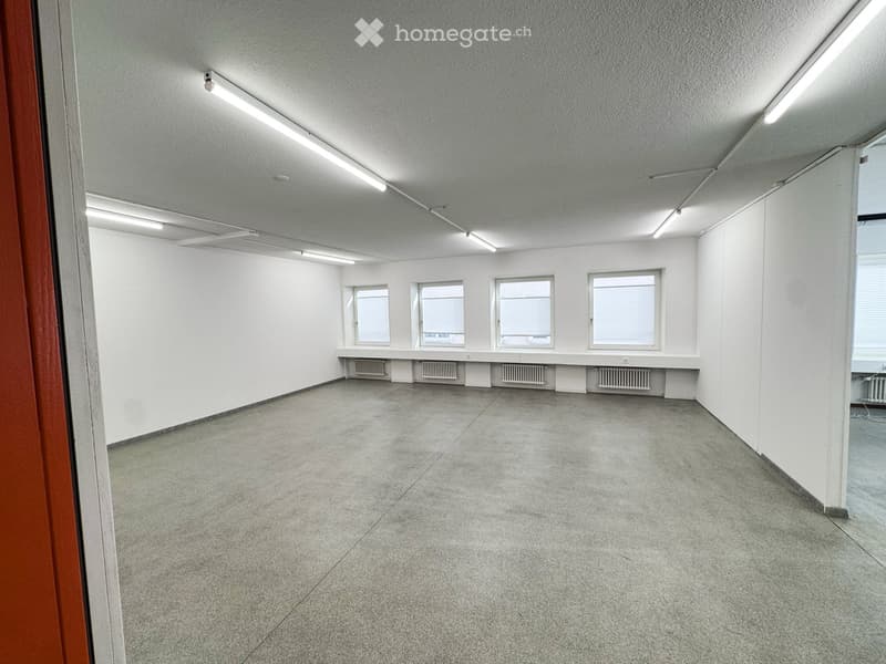 Empty room with white walls, concrete floor, and four windows with blinds. Radiators are visible under the windows.