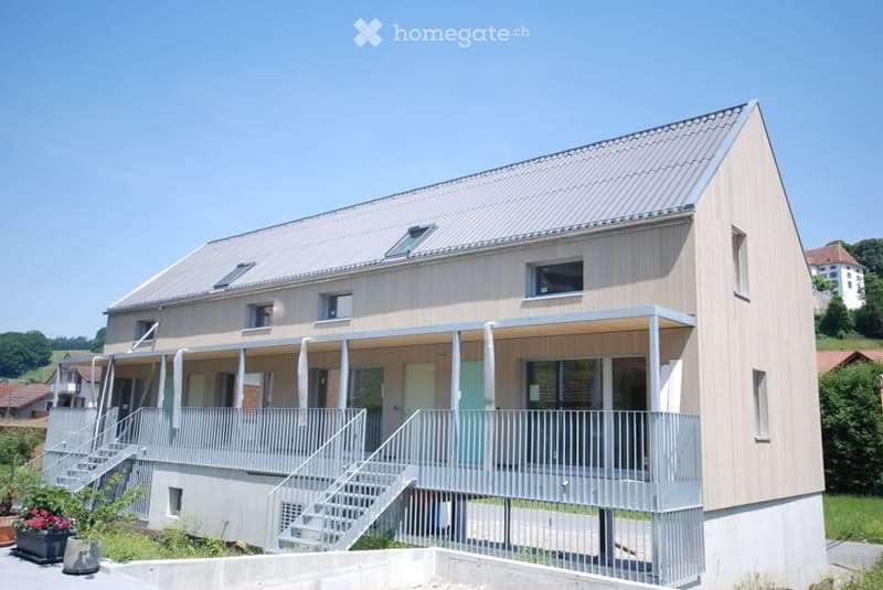 Modern two-story building with a flat roof, large windows, and a covered balcony area on the first floor.