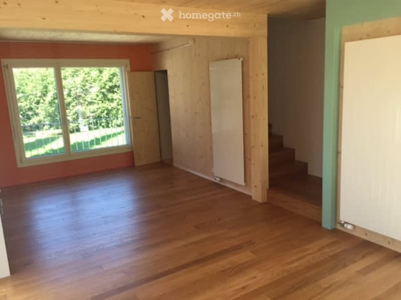 Empty room with wooden flooring, large window, and wooden walls. No furniture or equipment present.
