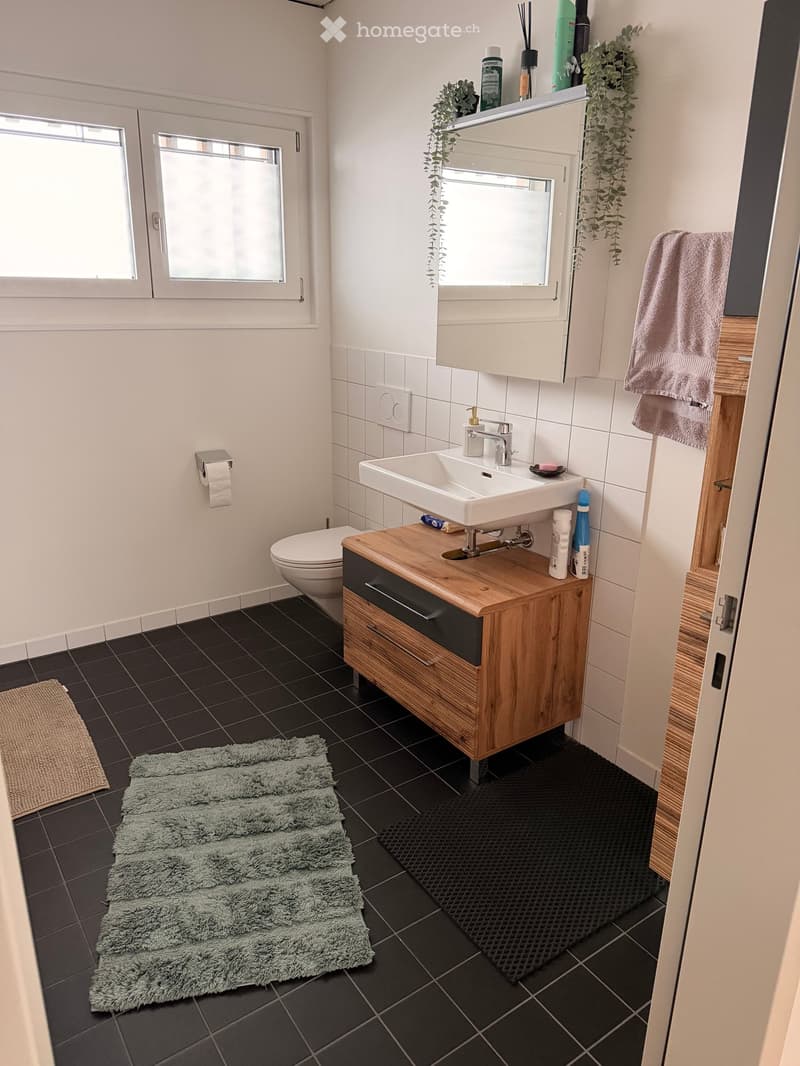 Modern bathroom with dark tiled floor, white walls, sink with wooden cabinet, toilet, mirror, and towels.