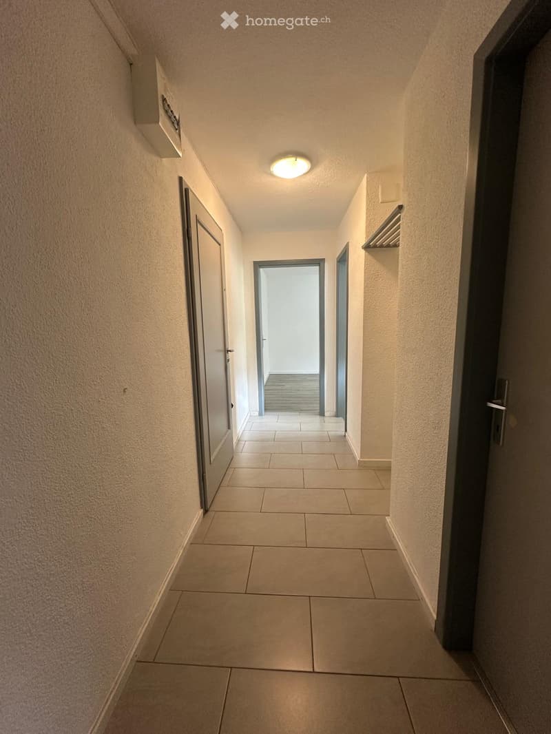 A clean, well-lit hallway with tiled flooring, beige walls, and several doors leading to different rooms.