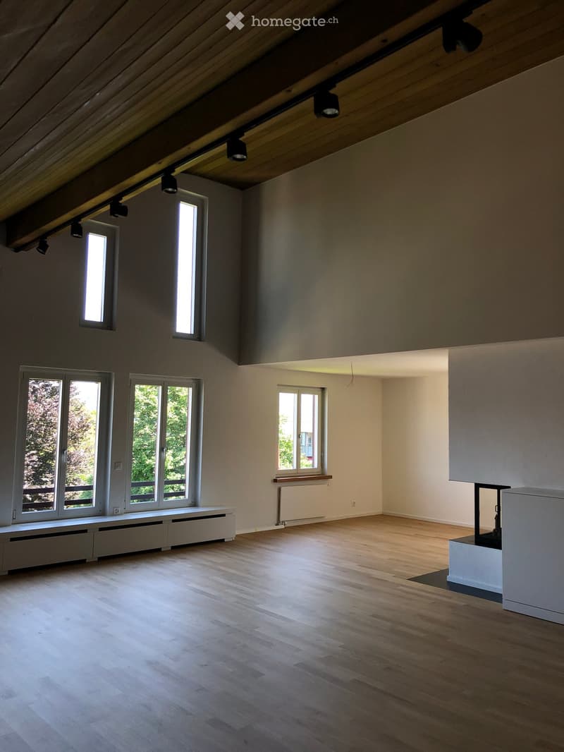 Empty attic room with wooden flooring, exposed wooden beams, and multiple windows allowing natural light. No furniture or furnishings are present.
