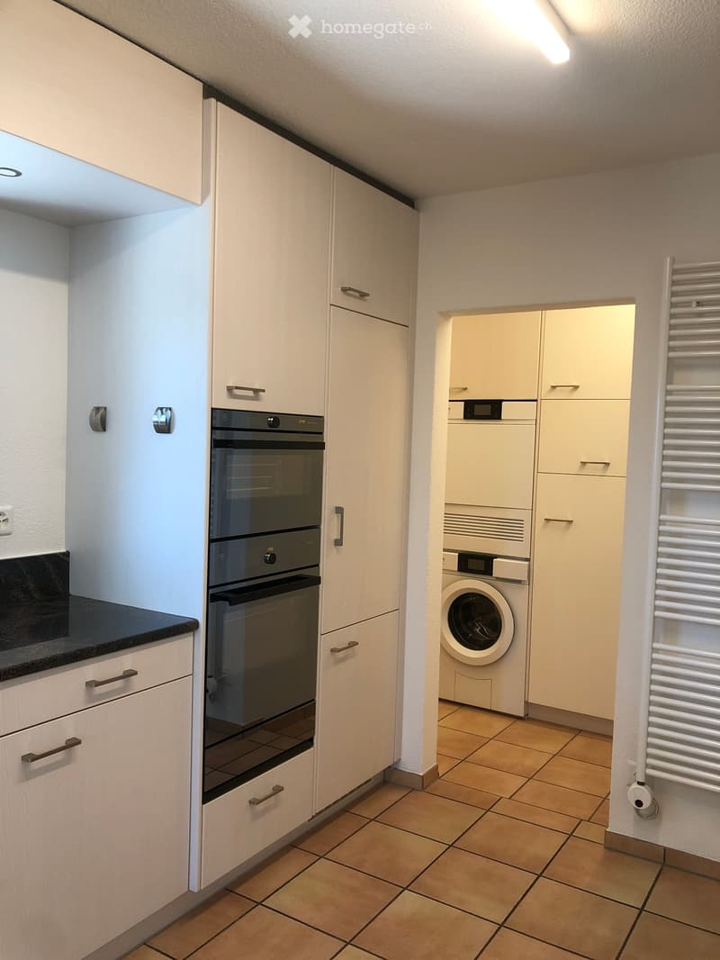 Modern kitchen with white cabinets, built-in oven, and adjacent laundry area with a washing machine and radiator.