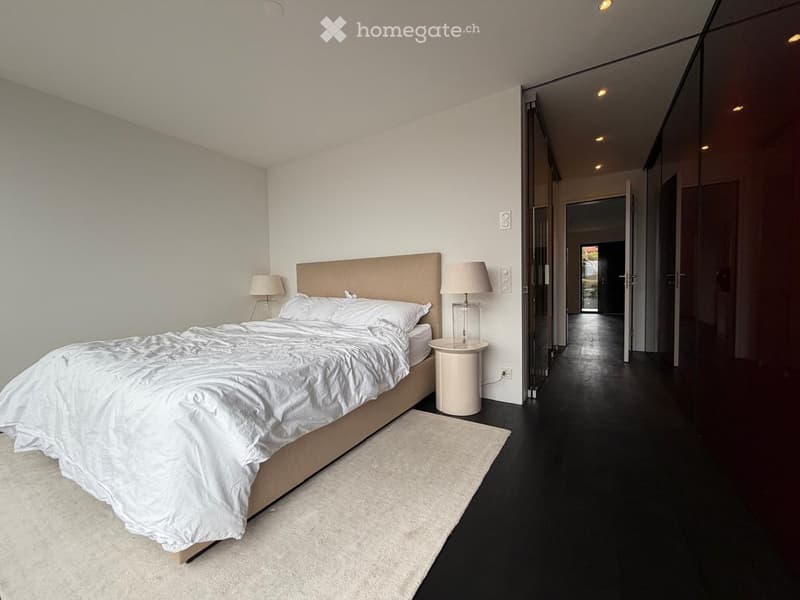 Modern bedroom with a large bed, white bedding, two nightstands with lamps, and a light-colored rug on the floor.