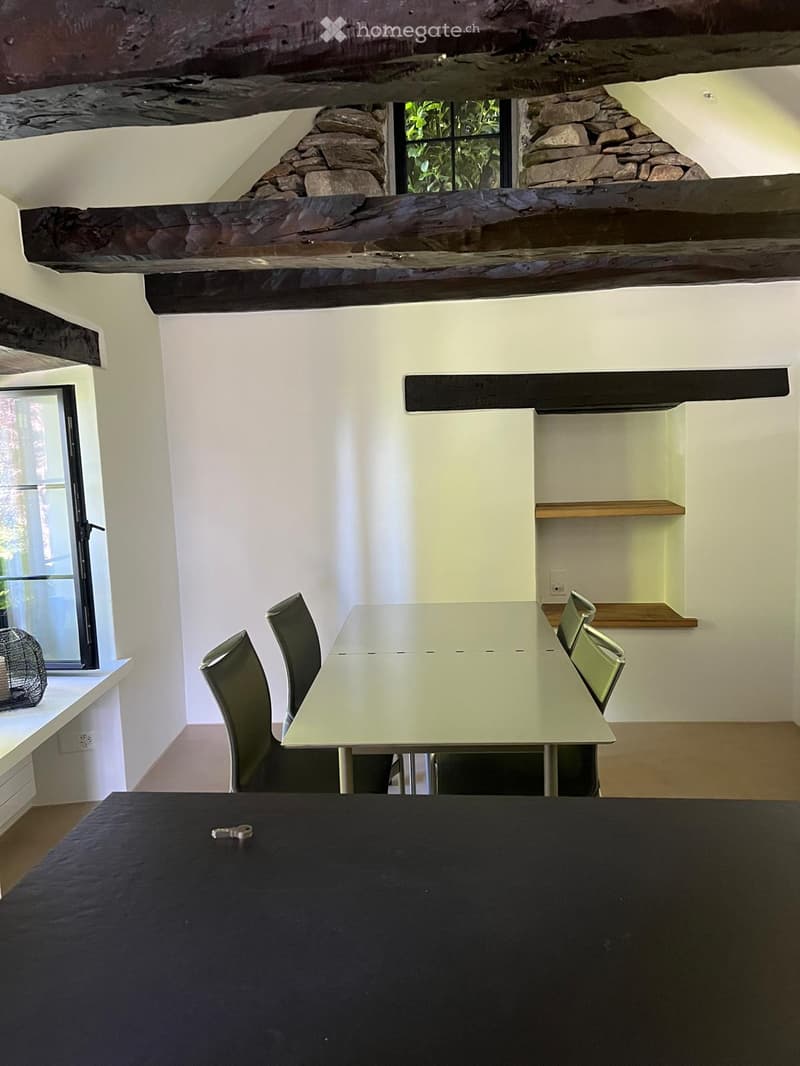 Dining area with a modern table, four chairs, and built-in shelving unit. Exposed wooden beams and stone accents on the walls.