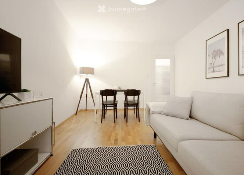 Modern living room with a white sofa, coffee table, dining table with chairs, floor lamp, TV, and picture frames on the wall.