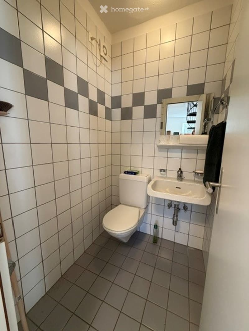 Small bathroom with white and grey checkered tiles, a toilet, a sink with a mirror above it, and a towel hanging on the side.