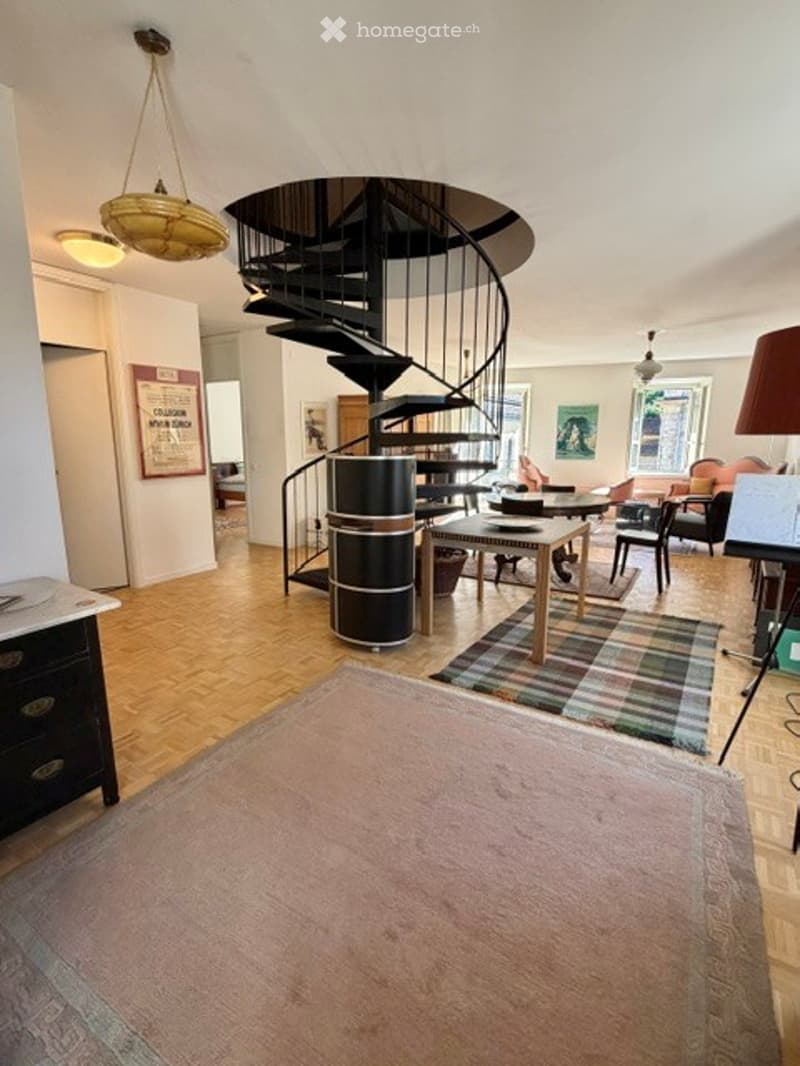 Spacious living room with wooden flooring, a spiral staircase, and modern furniture including a sofa, chairs, and a coffee table.