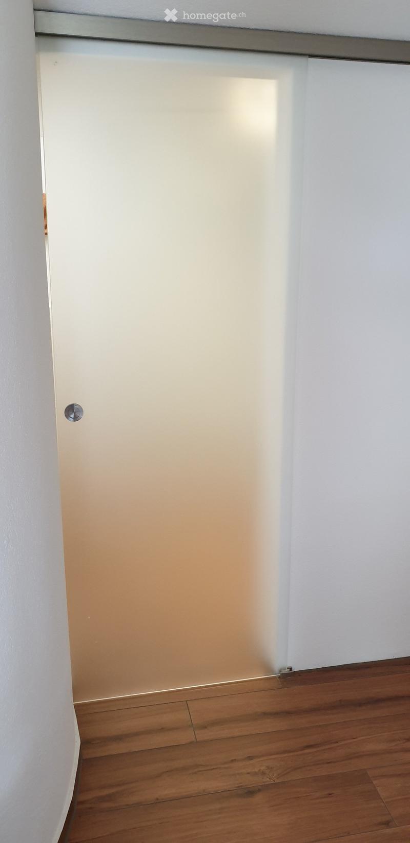 Empty room with wooden flooring and white walls, featuring a sliding glass door.
