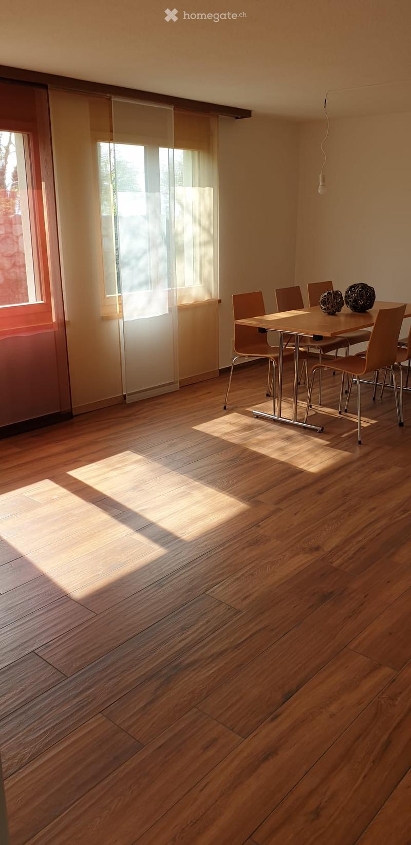 Bright dining area with wooden floor, large windows, dining table with chairs, and decorative spheres on the table.