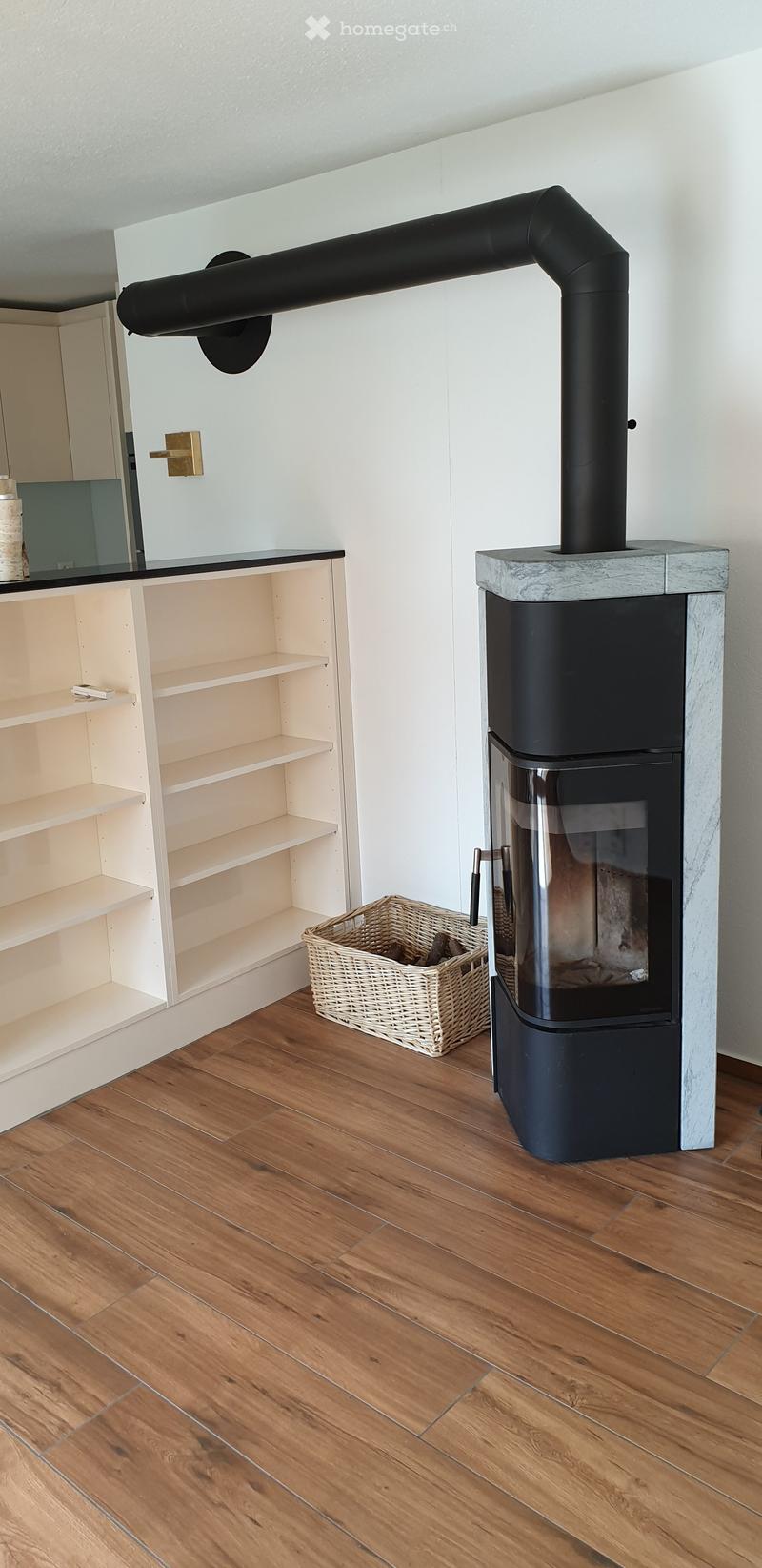 Modern living room with a sleek black wood-burning fireplace, a built-in shelf unit, and a wicker basket on the floor.