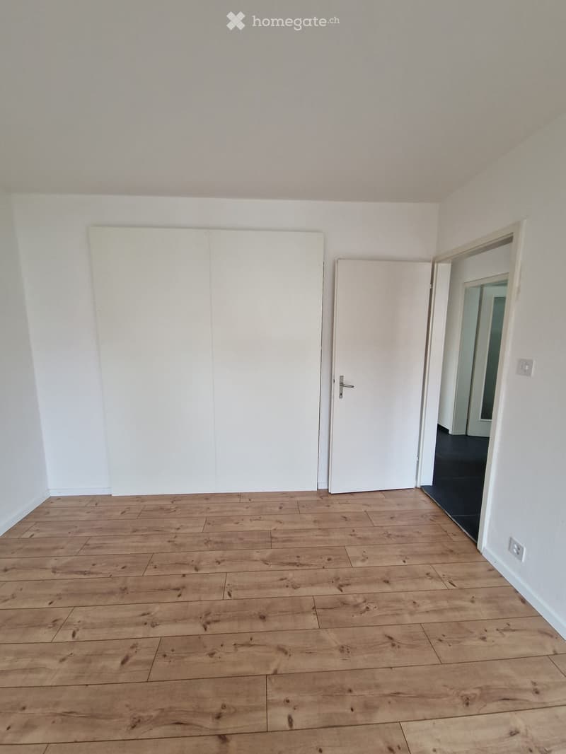 Empty room with white walls, wooden floor, white doors, power outlet, no furniture.