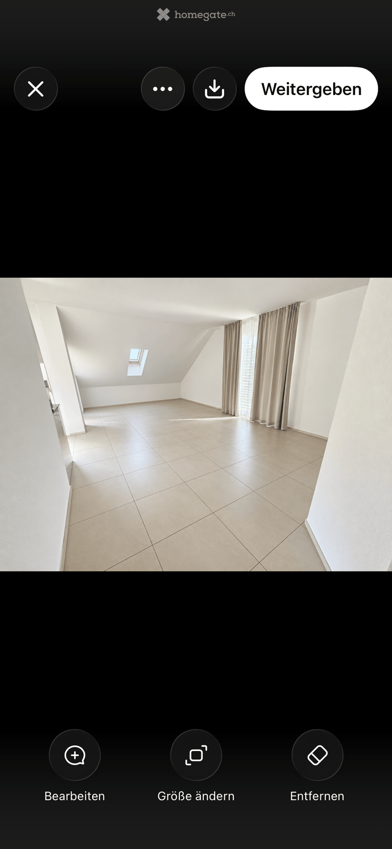 Empty attic room with tiled floor, white walls, skylight window, and beige curtains on a window.