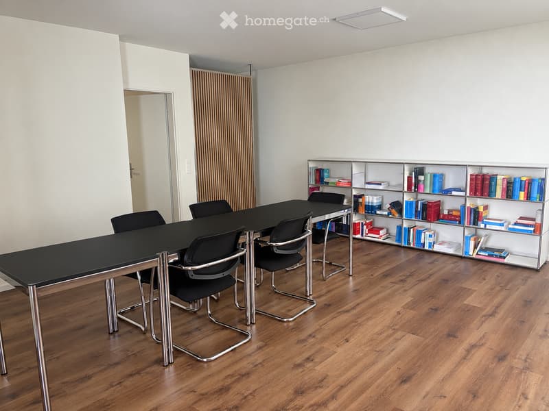Modern office or meeting room with a black table, several black chairs, and a bookshelf filled with books.