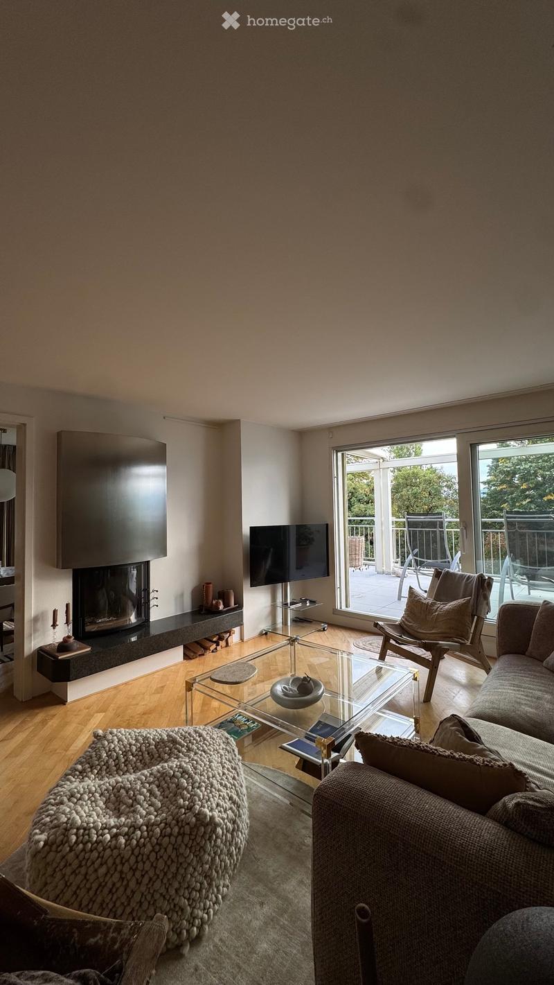 Modern living room with a grey sofa, glass coffee table, fireplace, and large windows opening to a balcony.