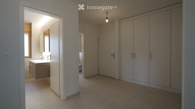 Empty room with tiled floor, white walls, built-in wardrobes, and an open doorway leading to a modern bathroom with a sink and mirror.