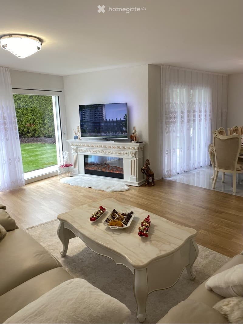 Elegant living room with a fireplace, large windows, a sofa, coffee table, and dining area with chairs and a table.