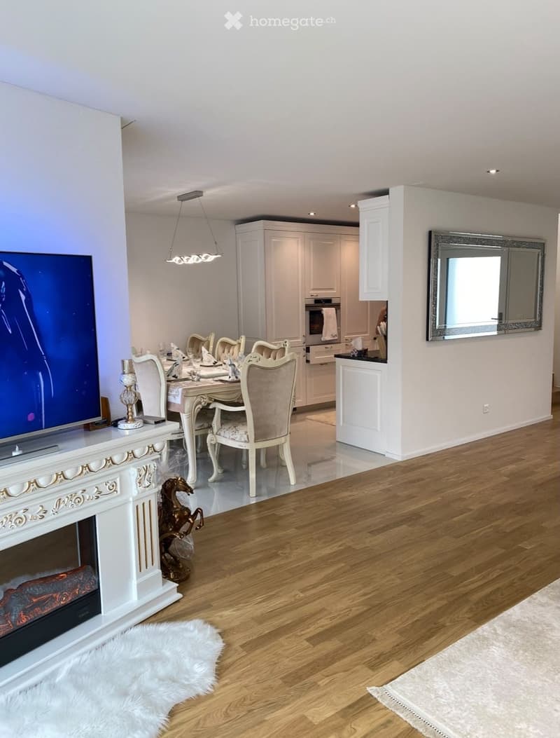 Open-plan living and dining area with a fireplace, television, dining set, and modern kitchen in the background.