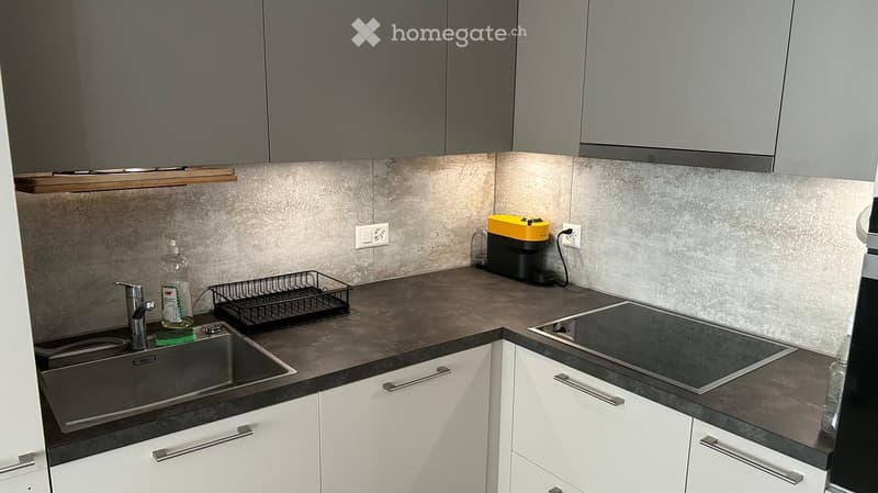Modern kitchen with grey cabinets, dark countertops, stainless steel sink, electric stove, and a coffee maker on the counter.