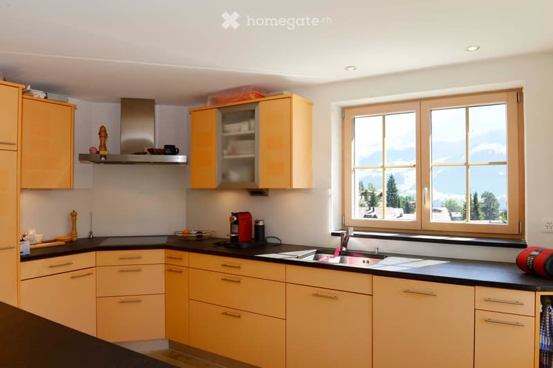 Modern kitchen with light wood cabinets, stainless steel appliances, and a large window offering a scenic mountain view.