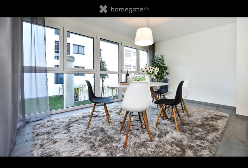 Modern dining area with large windows offering a view, a round white dining table surrounded by black and white chairs, a fluffy white rug, and a flower vase on the table.