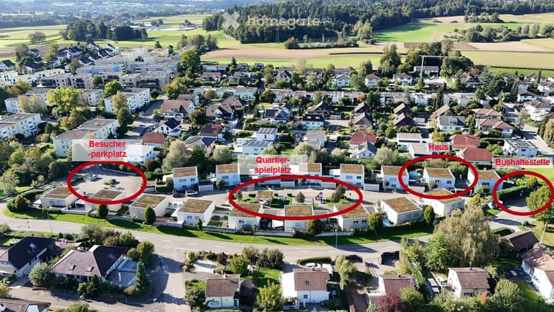 Aerial view of a residential neighborhood with multiple houses, green spaces, and a parking area.