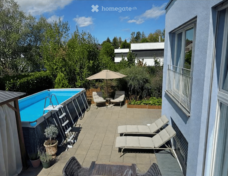 Outdoor patio area with a swimming pool, lounge chairs, umbrella, small table, and potted plants.