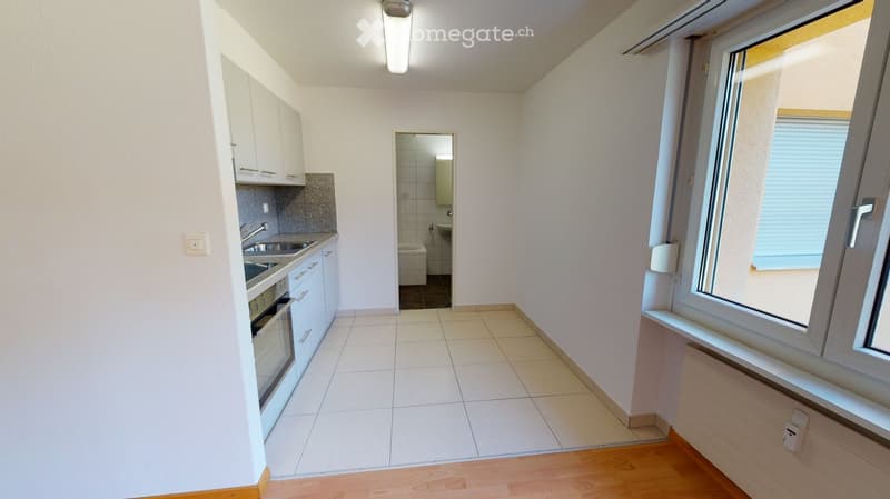 Modern kitchen with white cabinets, tiled floor, and a window. Includes a sink, oven, and faucet. Adjacent bathroom visible with a toilet and shower.