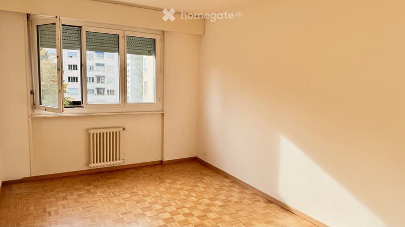 Empty room with wooden flooring, white walls, and large windows with blinds. A radiator is visible below the windows.