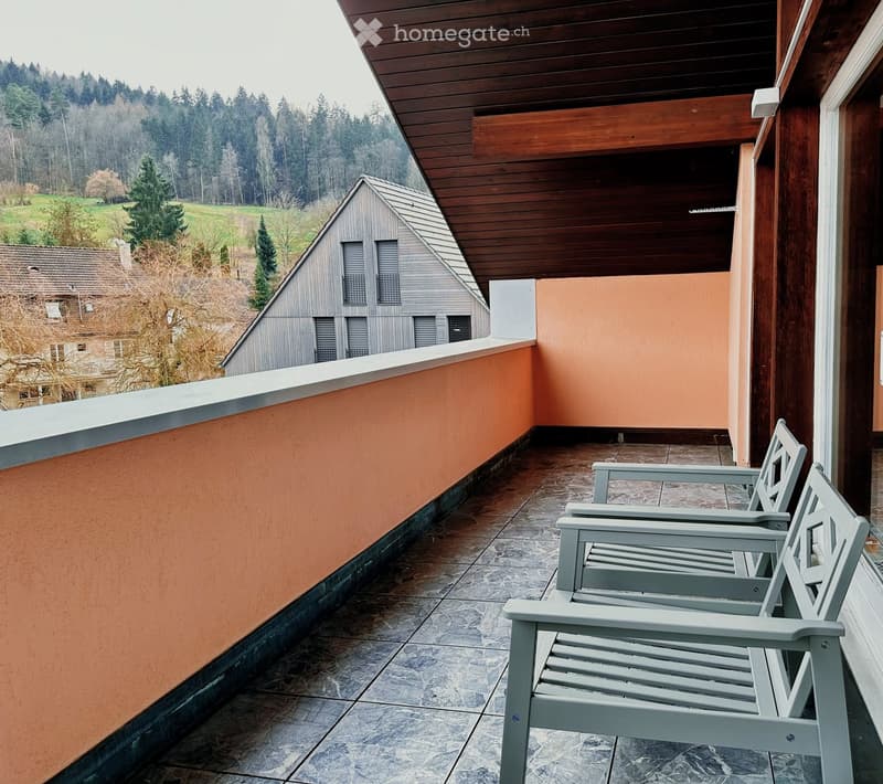 Balcony with wooden ceiling, stone floor, and two grey chairs, overlooking a scenic countryside view.