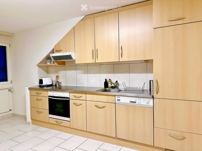 Modern kitchen with light wood cabinets, stainless steel appliances, and a tiled floor.