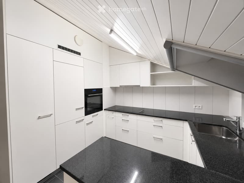 Modern kitchen with white cabinets, black countertops, stainless steel sink, and built-in oven.