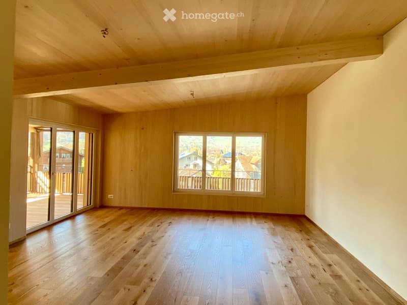 Empty room with wooden flooring, large windows, and sliding glass doors leading to a balcony.