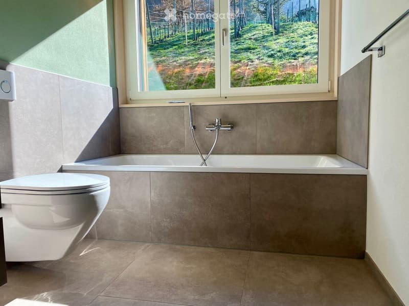 Modern bathroom with a bathtub, toilet, and large window offering a scenic view of a green landscape.